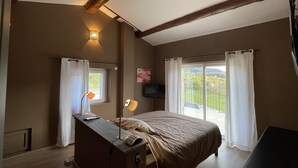 Ein Schlafzimmer mit Bett, Schreibtisch, Lampe, Fernseher und einem Balkon mit Vorhängen.