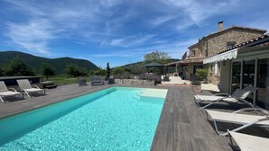Ein Swimmingpool mit Liegestühlen, ein Steinhaus und eine gebirgige Kulisse.