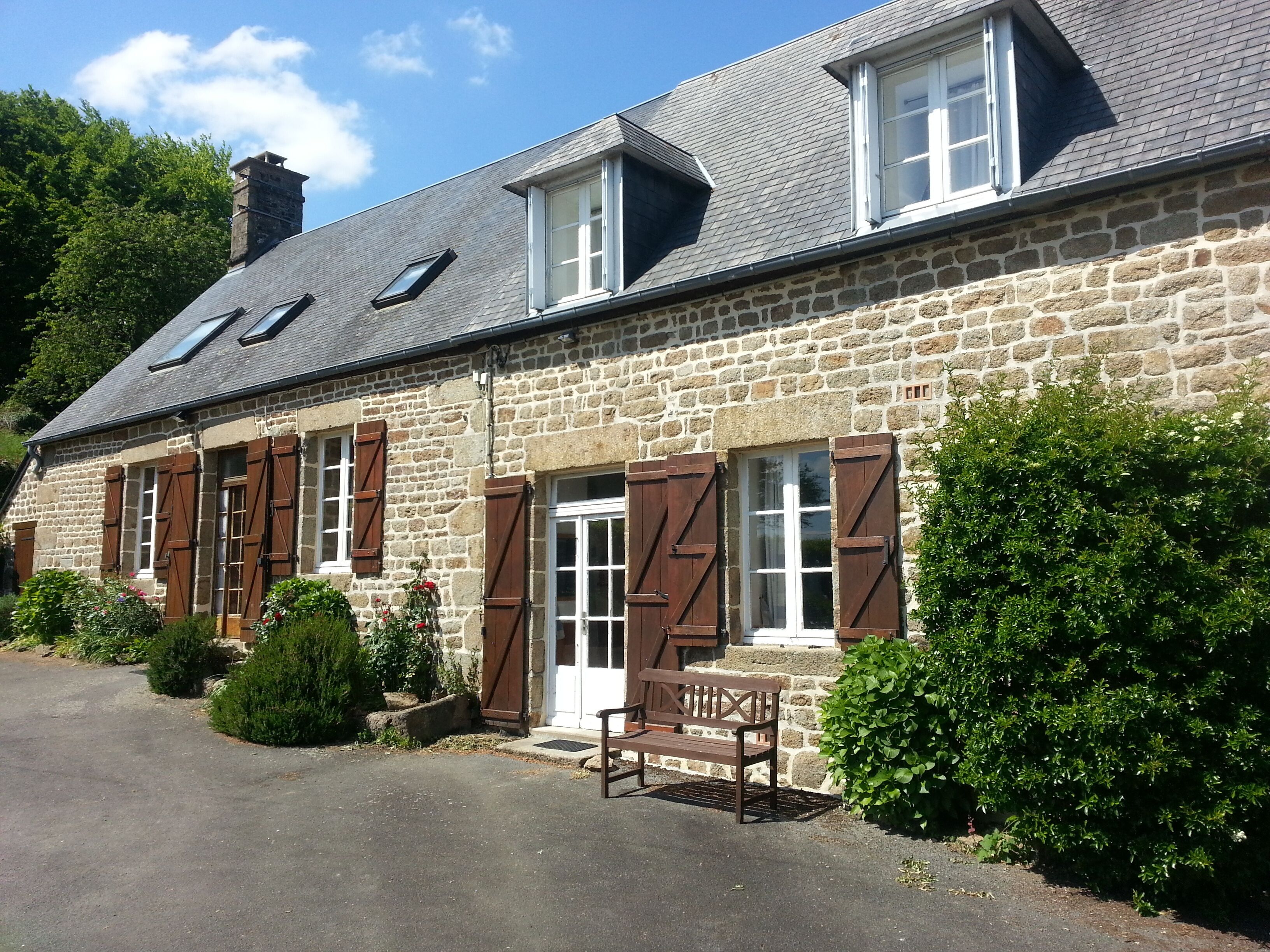 A stone building with a sloped roof, multiple windows with shutters, and a bench outside.