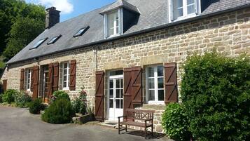 A stone building with a sloped roof, multiple windows with shutters, and a bench outside.