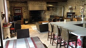 A rustic interior with a stone fireplace, wooden beams, and a dining area with a checkered tablecloth.