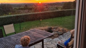 Two people seated at a table on a patio with a view of a sunset over a rural landscape.