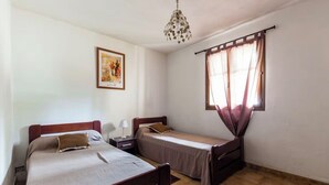 Ein Zimmer mit zwei Betten, einer Kristallleuchter, einem Fenster mit Vorhängen und einem gerahmten Bild an der Wand.