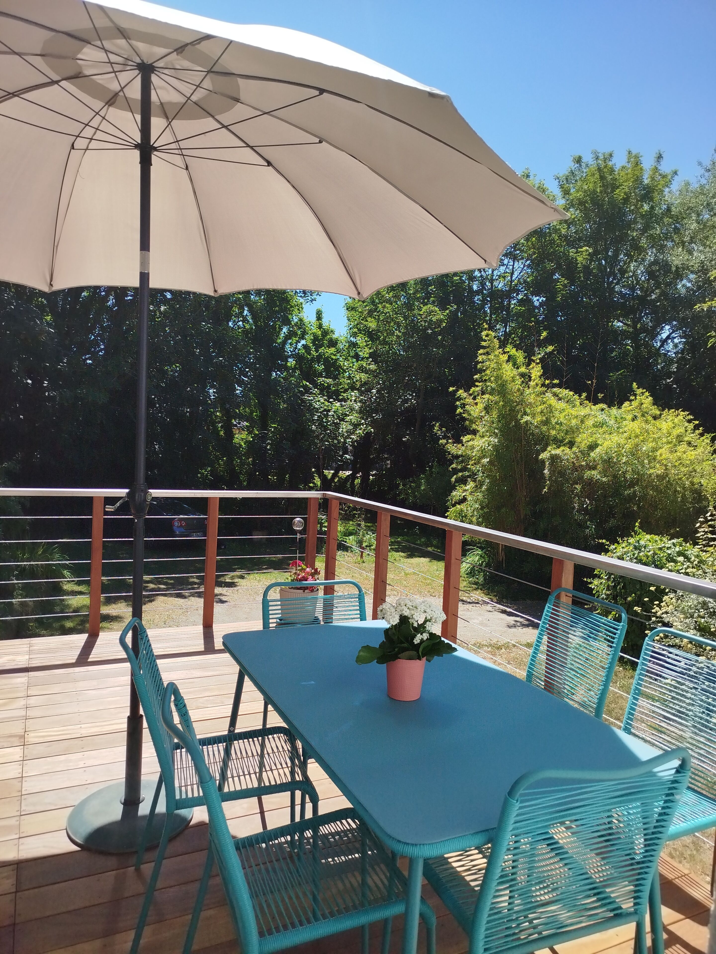 Eine Terrasse im Freien mit Tisch, Stühlen, Sonnenschirm und Geländer mit Blick auf einen Garten.