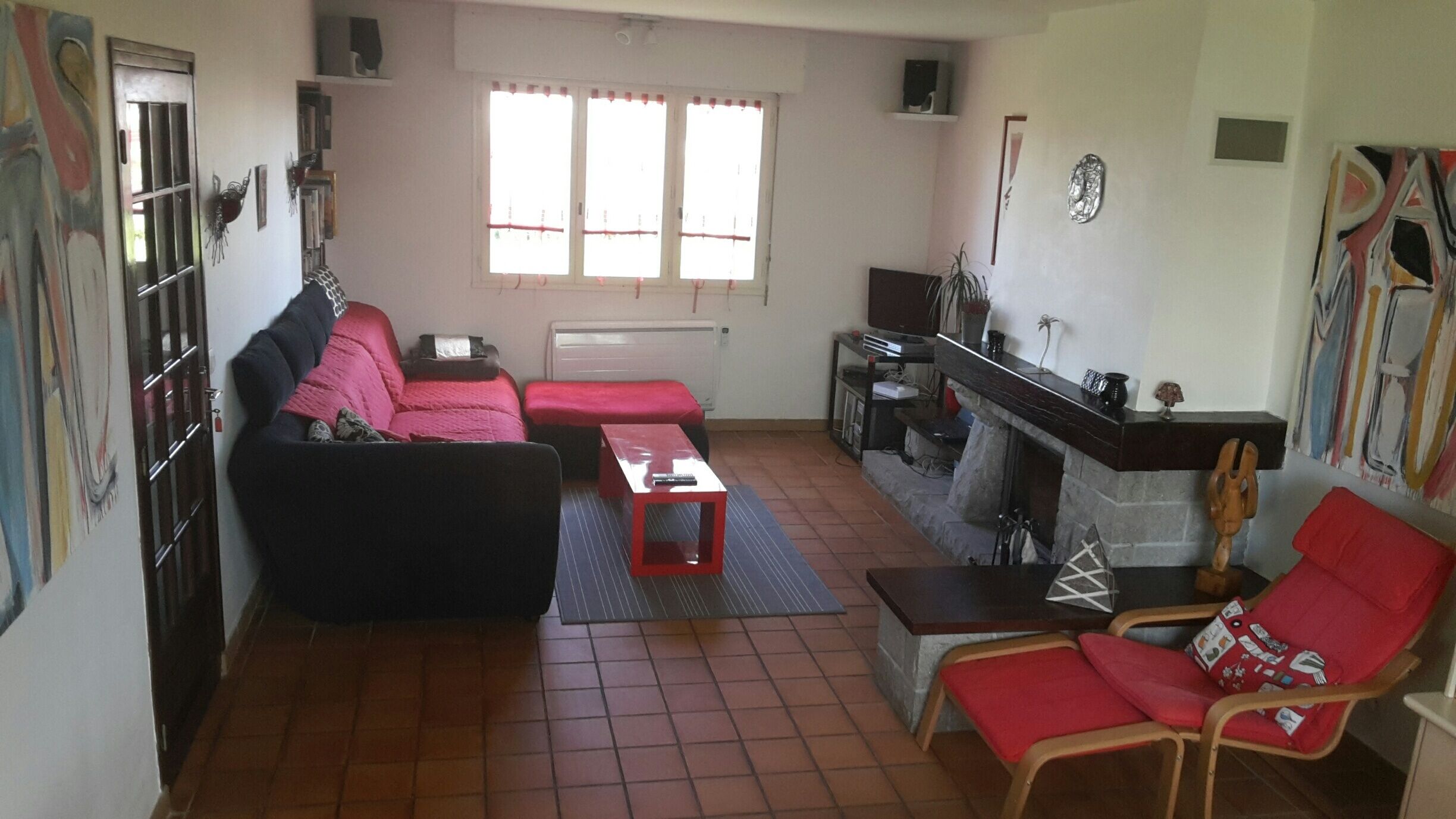 Una sala de estar con sofá, sillón rojo, mesa de centro, chimenea y televisión.