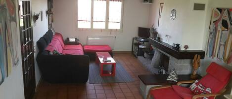 Una sala de estar con sofá, sillón rojo, mesa de centro, chimenea y televisión.