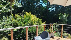 Eine Holzterrasse mit Plastikstühlen und einem Tisch, umgeben von einem Metallgeländer und Pflanzen.