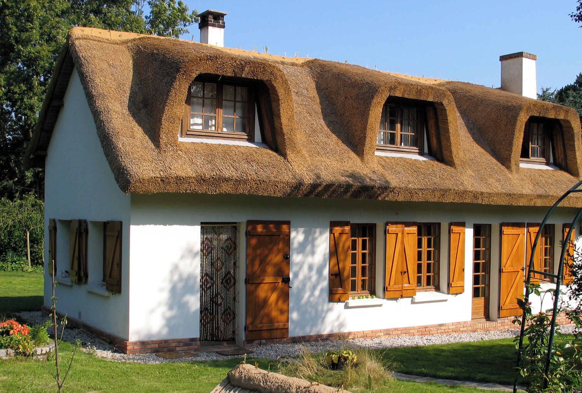 Une maison traditionnelle avec un toit de chaume, des murs blancs et des volets en bois.