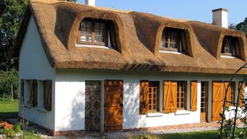 Une maison traditionnelle avec un toit de chaume, des murs blancs et des volets en bois.