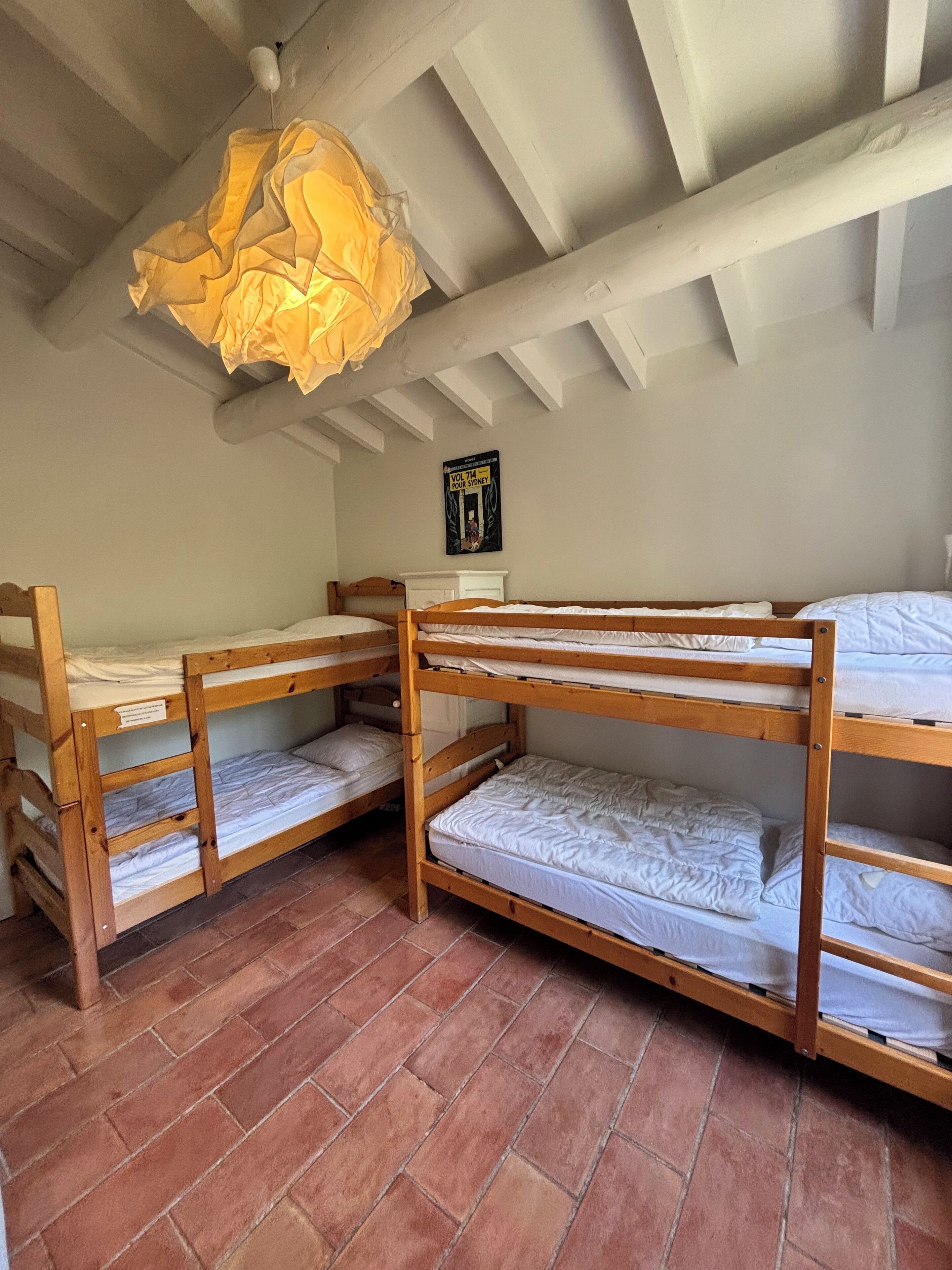A dormitory room with bunk beds, a brick floor, and a ceiling light fixture.