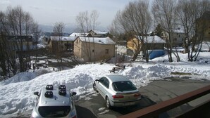 A residential area with snow-covered ground, parked cars, and houses with snow on roofs.