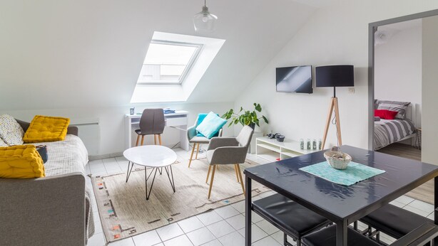 A modern, well-lit room with a loft bed, a dining table, and a TV.