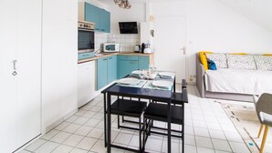 A compact kitchen with teal cabinets, a dining table set for four, and a bed with a patterned cover.