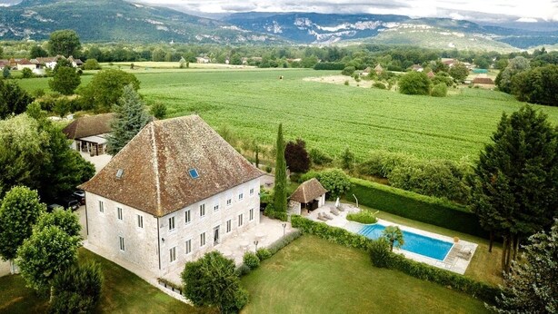 Un grande edificio in pietra con piscina, immerso in campi verdi e alberi.