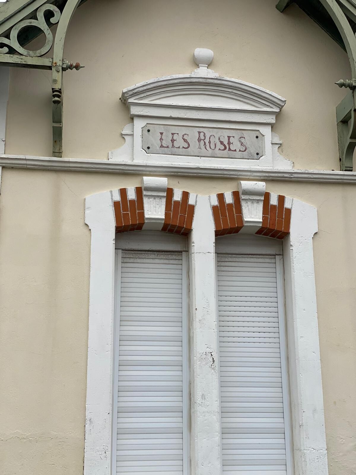 A building facade with a sign reading "LES ROSES" above two closed shutters.