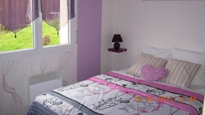 Une chambre à coucher avec un lit, une fenêtre avec des rideaux, une table de chevet avec une lampe et un élément décoratif mural.
