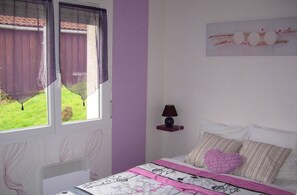 Een slaapkamer met een bed, een raam met gordijnen, een nachtkastje met een lamp en een wanddecoratie.