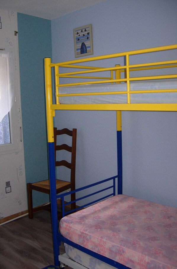 Ein Stockbett mit einem Holzstuhl, ein Fenster mit Jalousien und eine Wand mit einem gerahmten Bild.