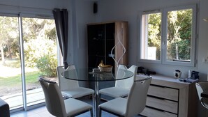 A modern dining area with a glass table and white chairs, a wooden cabinet, and a view of the outdoors. - CHARMING VILLA WITH PRIVATE POOL 4 TO 5 PEOPLE NEAR PALOMBAGGIA (PORTO VECCHIO)