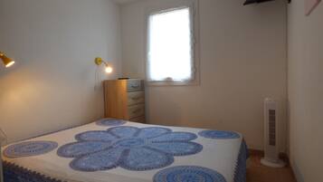 Een slaapkamer met een bed, een dressoir, een raam en een ventilator aan de muur.