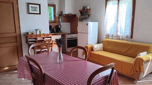 Ein gemütlicher Wohnbereich mit Esstisch, Stühlen, einer Couch, einer Küchenzeile und einem Fenster mit Vorhängen.