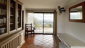 Une pièce dotée d’une grande porte-fenêtre coulissante donnant sur un balcon, d’une chaise en bois, d’un bureau blanc et d’une bibliothèque.