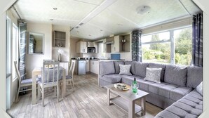 Uma sala de estar moderna com um sofá cinzento, uma mesa de centro de madeira e uma área de jantar com uma cadeira e mesa.