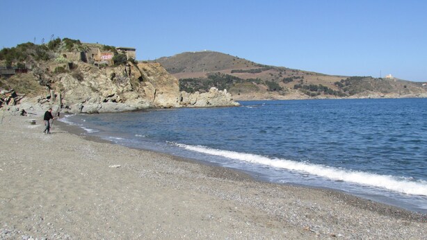 Una playa con terreno rocoso y un edificio en una colina.