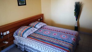 Una cama individual con una colcha estampada, una mesita de noche con lámpara y un aire acondicionado instalado en la pared.