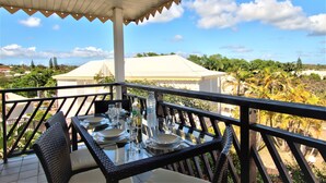 Un comedor con una mesa dispuesta para cuatro, con vistas a un paisaje exuberante de palmeras y un edificio blanco a lo lejos.