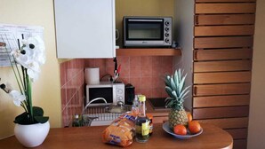 Una cocina con microondas, un fregadero, estufa y encimera con una bolsa de papas fritas, una botella y un plato de fruta.