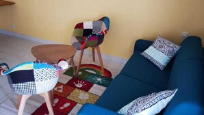 Una sala de estar con un sofá azul, sillas coloridas, un tapete estampado y un aire acondicionado instalado en la pared.