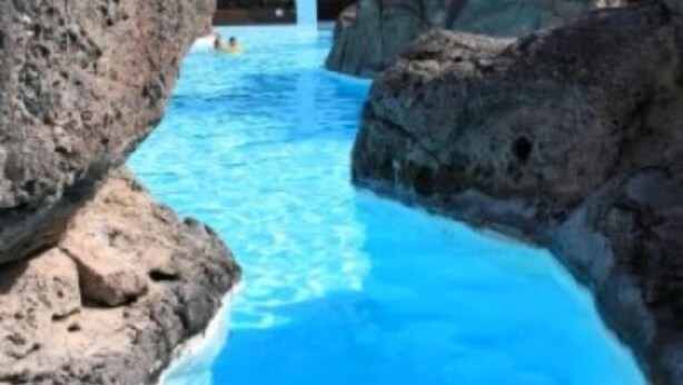 Una piscina con agua azul cristalina, rodeada de rocas grandes y palmeras.