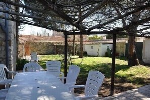 Un espace extérieur aménagé, abrité et doté de tables et de chaises, entouré d’arbres et offrant une vue sur un quartier résidentiel.