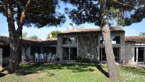 Un edificio de piedra de dos pisos con techo de tejas, un patio con sillas y un jardín con césped.