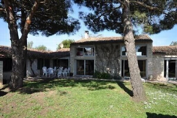 Un bâtiment en pierre de deux étages, avec un toit en tuiles, une terrasse avec des chaises et une cour gazonnée.