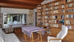 Una habitación con una amplia estantería, una mesa con mantel, una silla blanca y una ventana con vistas a árboles.