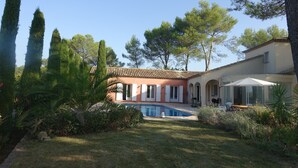 A house with a swimming pool, surrounded by tall trees and a well-maintained garden.