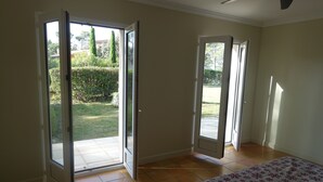 A bedroom with a bed, two open sliding glass doors leading to a patio, and a tiled floor.
