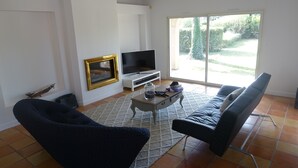 A living room with a sofa, a chair, a TV, and a sliding glass door leading to a garden.