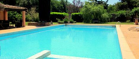 Une piscine rectangulaire bordée de carreaux, entourée d’une terrasse en briques et d’une végétation luxuriante.