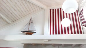 A high-ceilinged room with a striped wall, a hanging light fixture, and a small sailboat model.