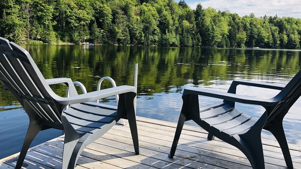 A wooden dock with two Adirondack chairs facing a calm lake surrounded by dense forest. - LAKEFRONT (private quay)-SPA-BILLARD-PING PONG-WORKING TABLE (Mille-Isles)