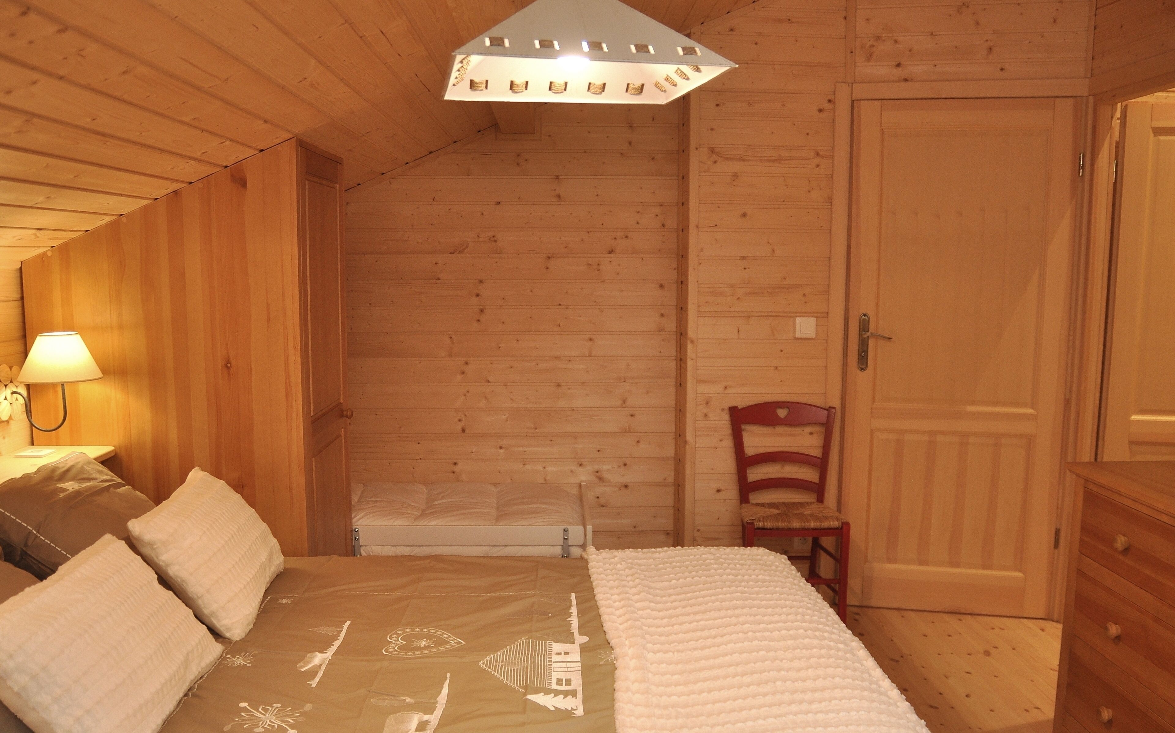 A wooden room with a bed, a chair, a lamp, and a door.
