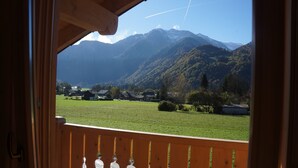 A view from a balcony with a wooden railing, overlooking a green field and a mountain range. - 50m from the ski bus, slopes 5min, 4 * Family Chalet with parking and Wifi (Samoëns)