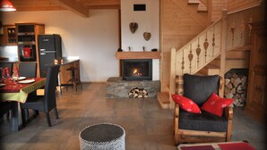 A cozy living room with a fireplace, a dining area with a table set for two, and a staircase leading to an upper level. - 50m from the ski bus, slopes 5min, 4 * Family Chalet with parking and Wifi (Samoëns)