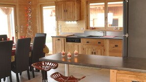 A wooden cabin interior with a dining area, two stools, a kitchen with wooden cabinets, and a refrigerator. - 50m from the ski bus, slopes 5min, 4 * Family Chalet with parking and Wifi (Samoëns)