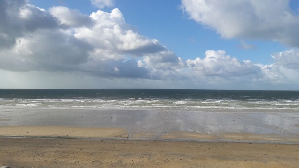 Una playa con arena y cielo despejado con nubes.
