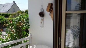 Una silla blanca al aire libre en un balcón con baranda blanca, un termómetro y una decoración cono de pino.