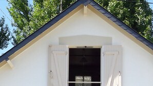 Un edificio blanco con techo a dos aguas y una ventana con contraventanas blancas.